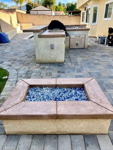 Backyard patio with a stone fire pit and a rectangular fire feature filled with blue glass stones.