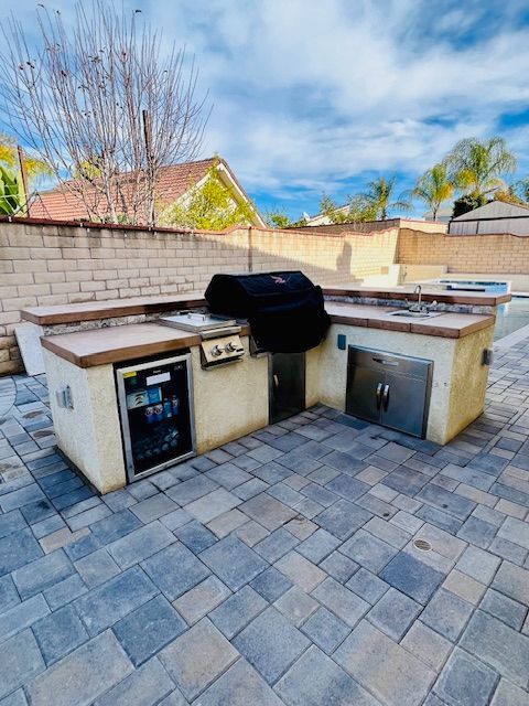 Outdoor stone kitchen with built-in grill, sink, and cabinets under a blue sky