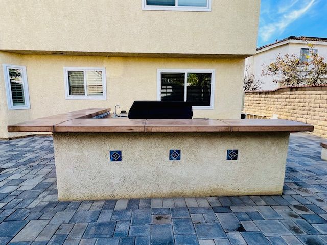 Outdoor patio with a built-in barbecue grill and beige stucco wall in a paved courtyard