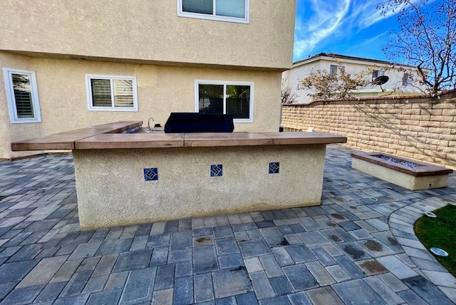 Backyard patio with paver stones, a built-in grill island, and a stone bench against a brick wall.