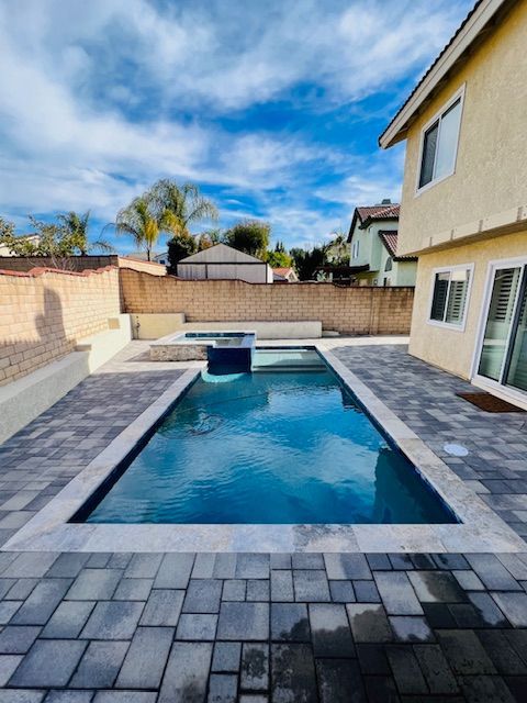 Backyard pool with stone patio beside a beige house under a blue sky