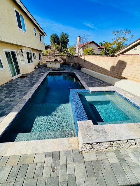 Backyard swimming pool with blue water, tiled deck, and beige house walls on either side