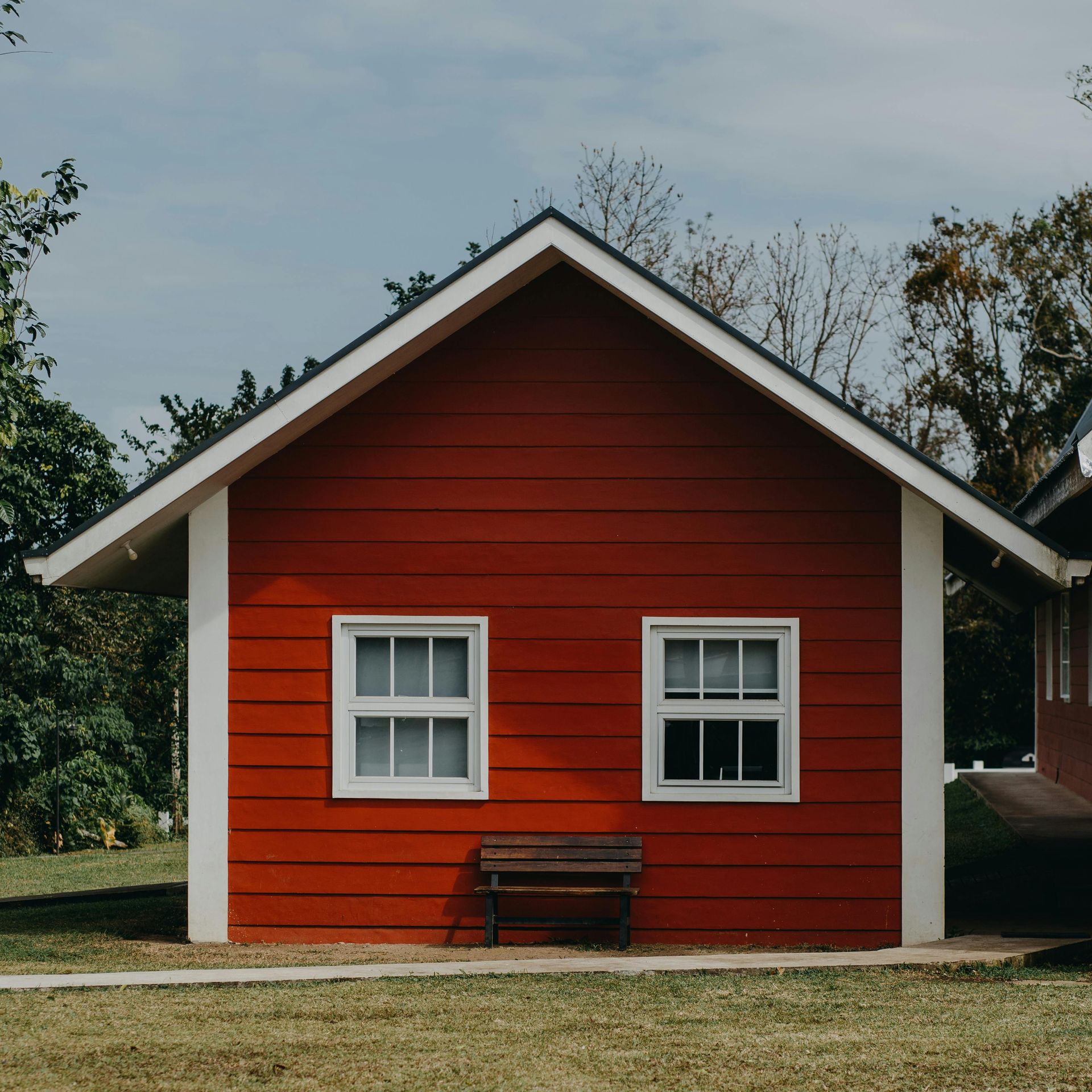 Red house with white trim and two windows, fronted by a bench on a grassy yard.
