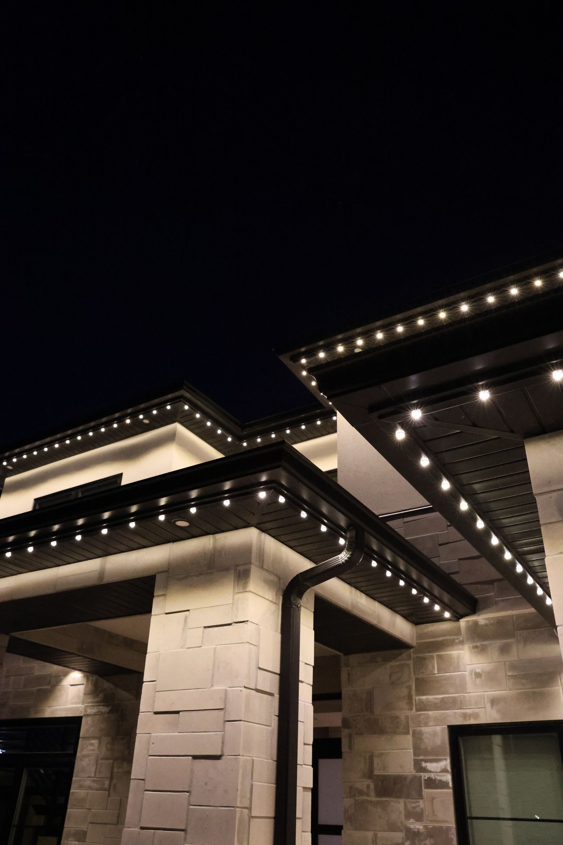 Illuminated stone house roofline and columns at night with warm eave lights against a dark sky