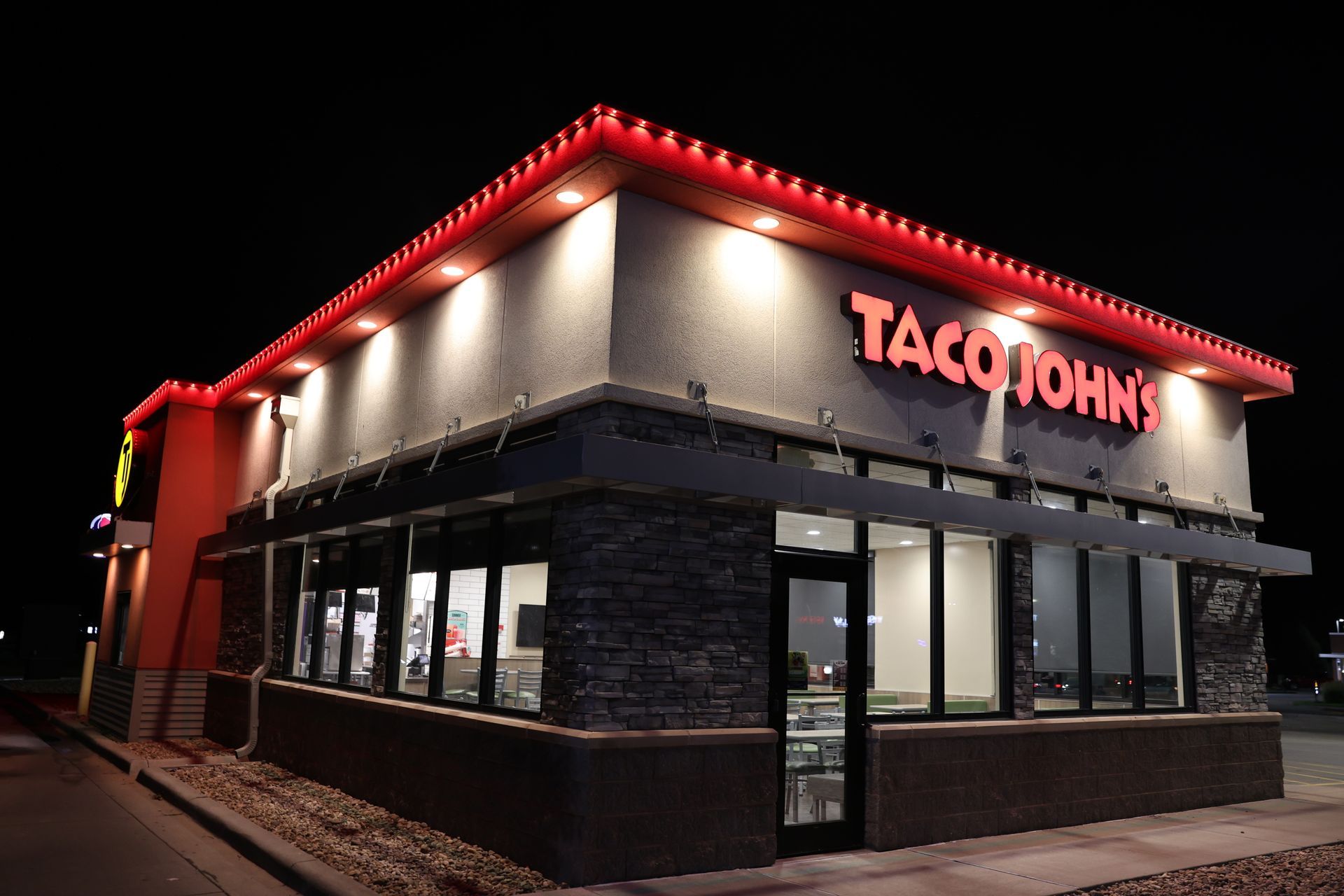 Taco John's fast-food restaurant at night, with red roof lights and illuminated windows