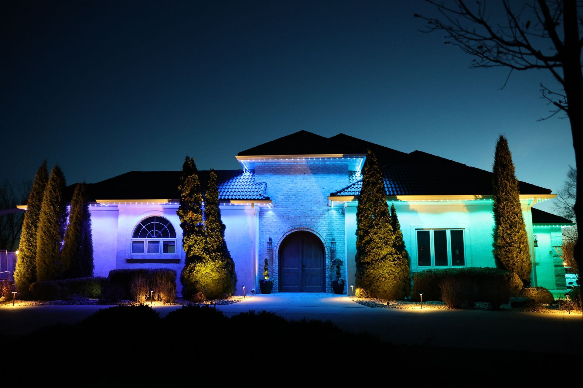 Single-story house at night, illuminated in blue, purple, and green lights, with a dark sky above.