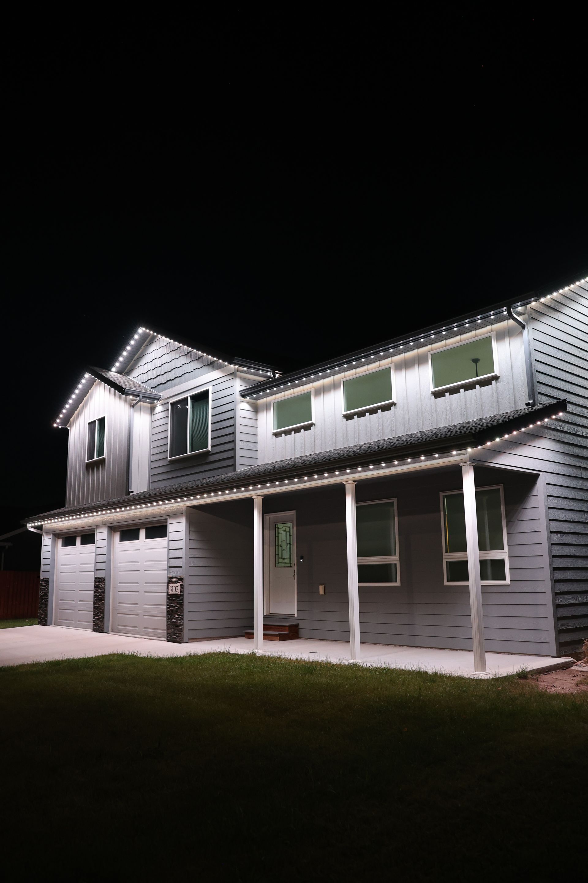 Lit two-story house with white siding and porch at night