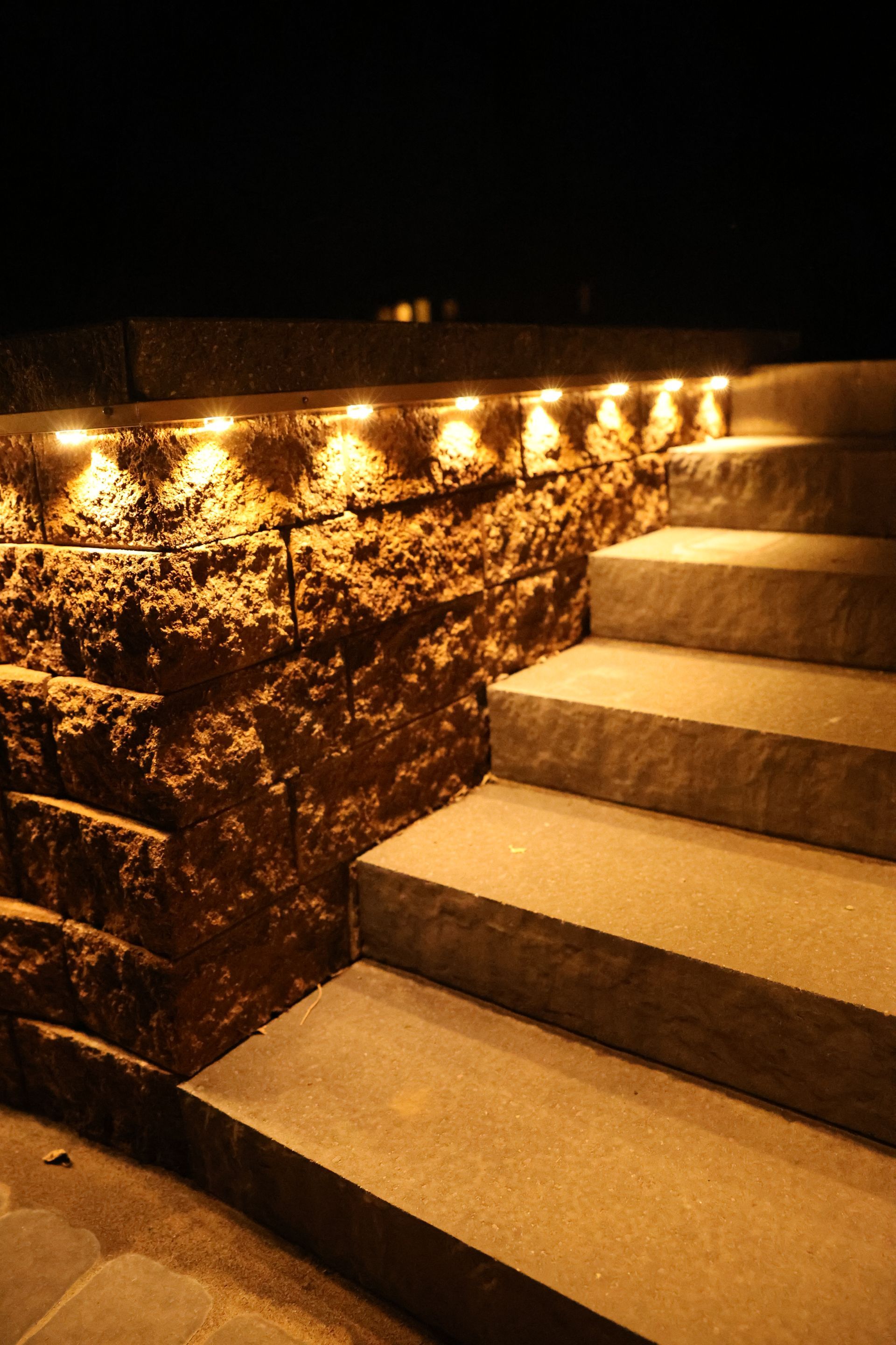 Stone steps beside a lit rock wall at night, with warm amber lights along the edge