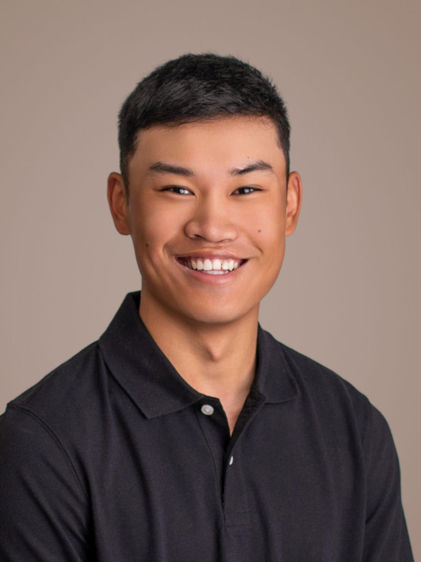 Smiling person in a black collared shirt against a plain beige background
