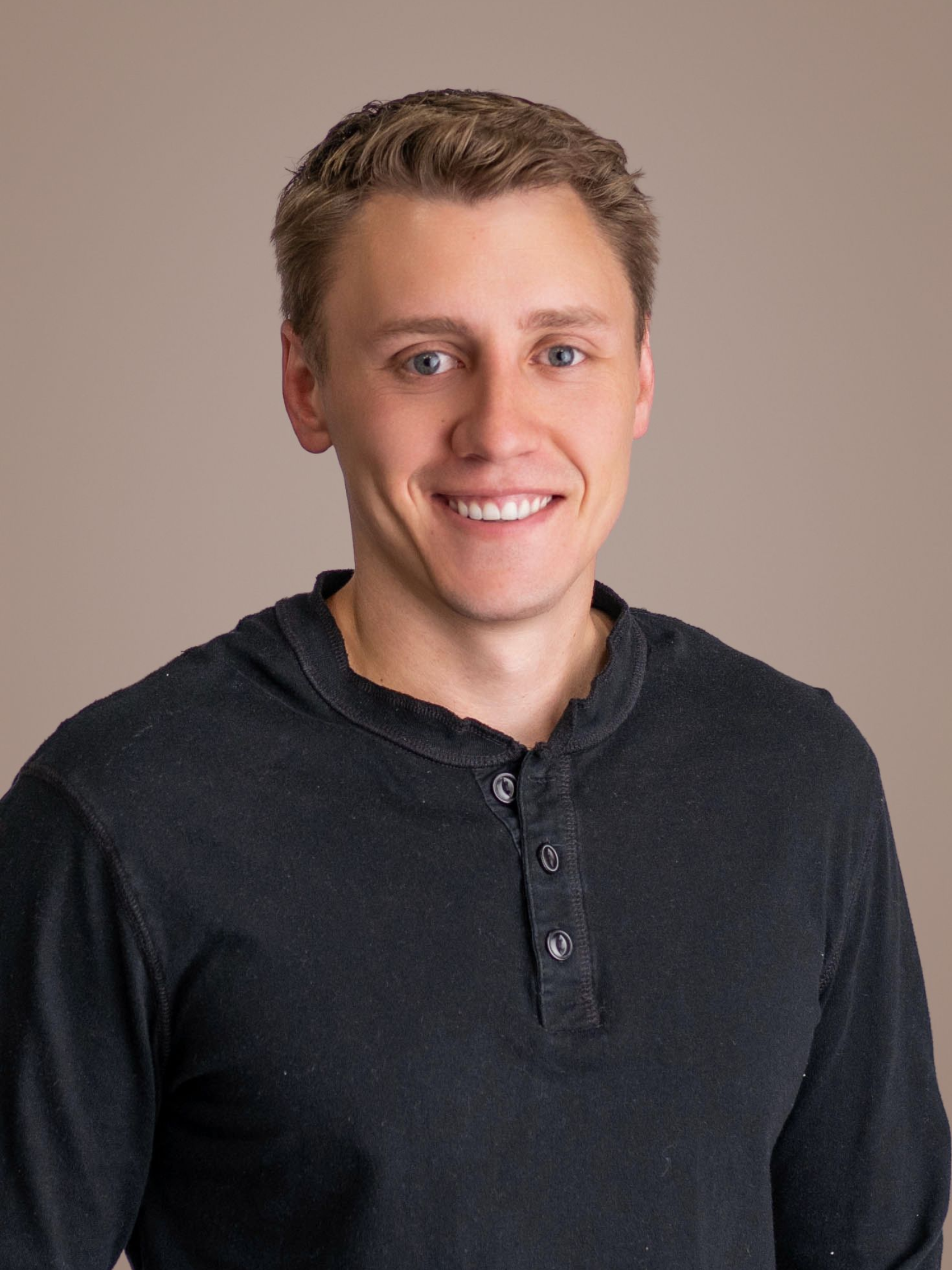 Smiling man in a dark gray henley shirt against a plain beige background