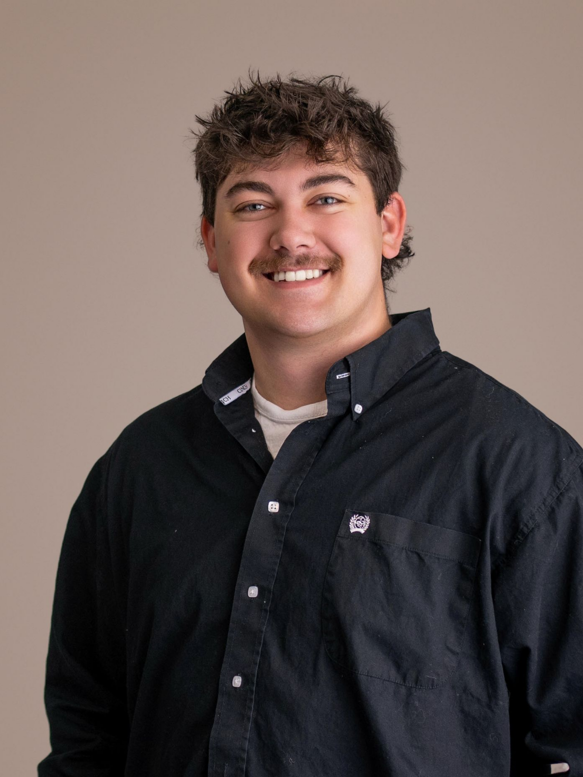 Smiling person in a black button-up shirt against a plain beige background