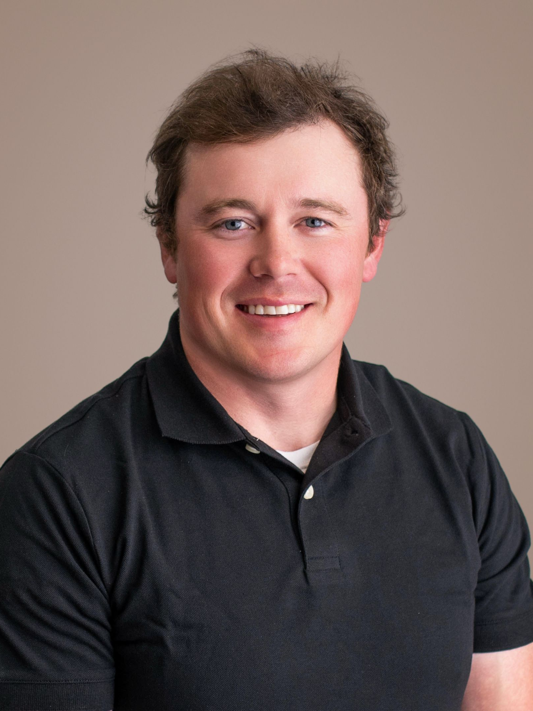 Smiling person in a dark polo shirt against a plain beige background