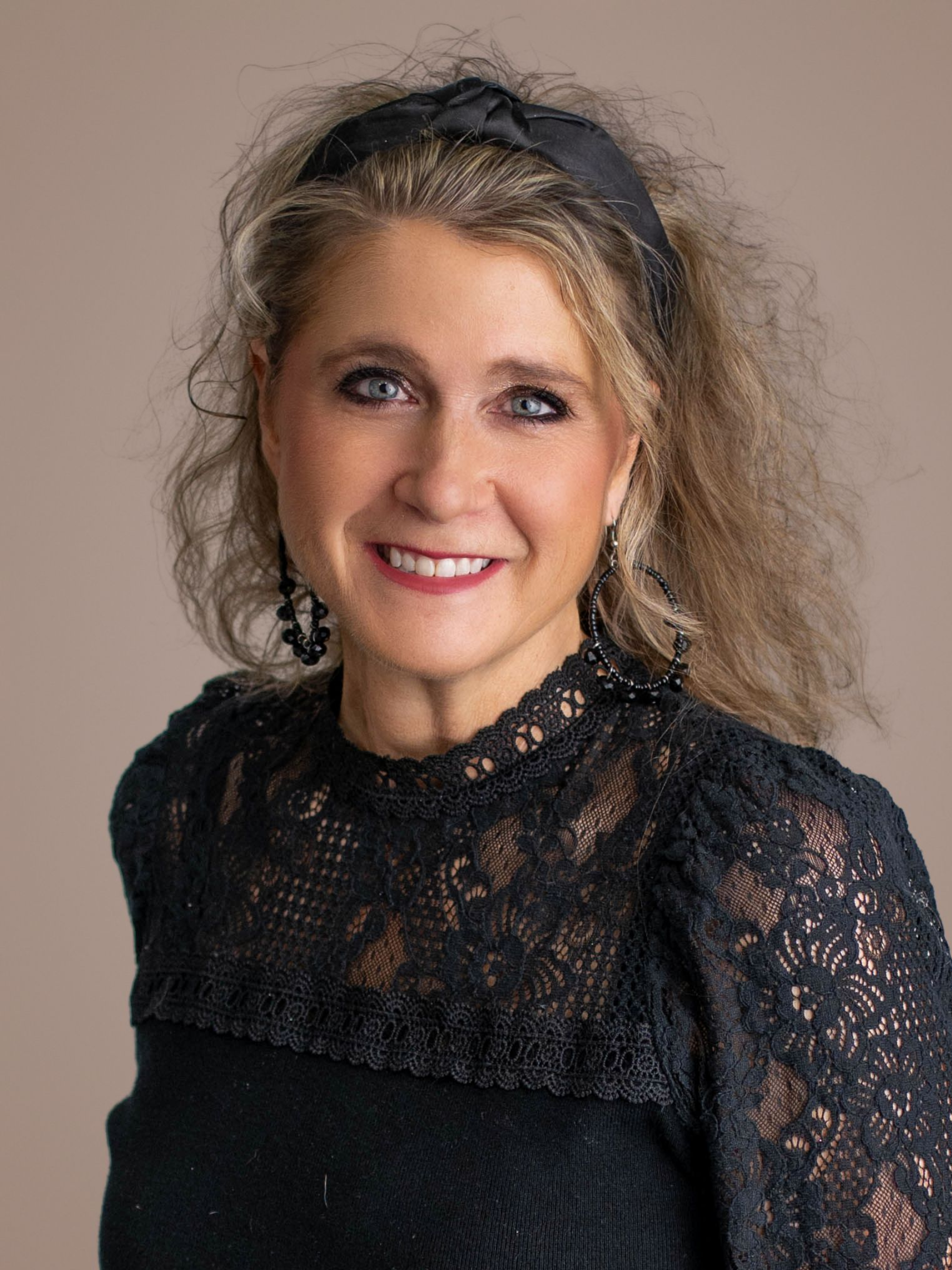Smiling woman in a black lace top against a neutral background