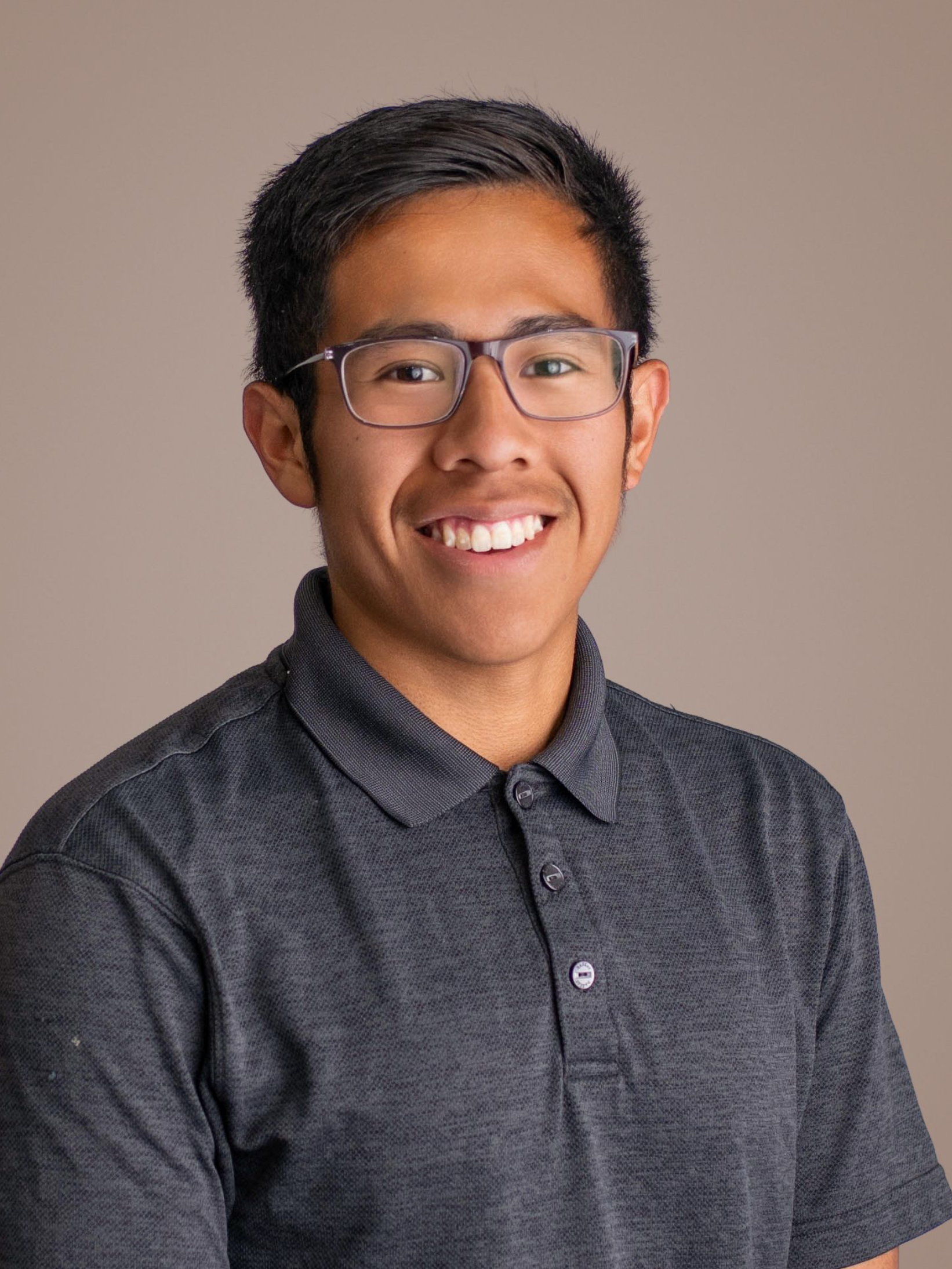 Smiling person in glasses wearing a dark gray polo shirt against a plain beige background