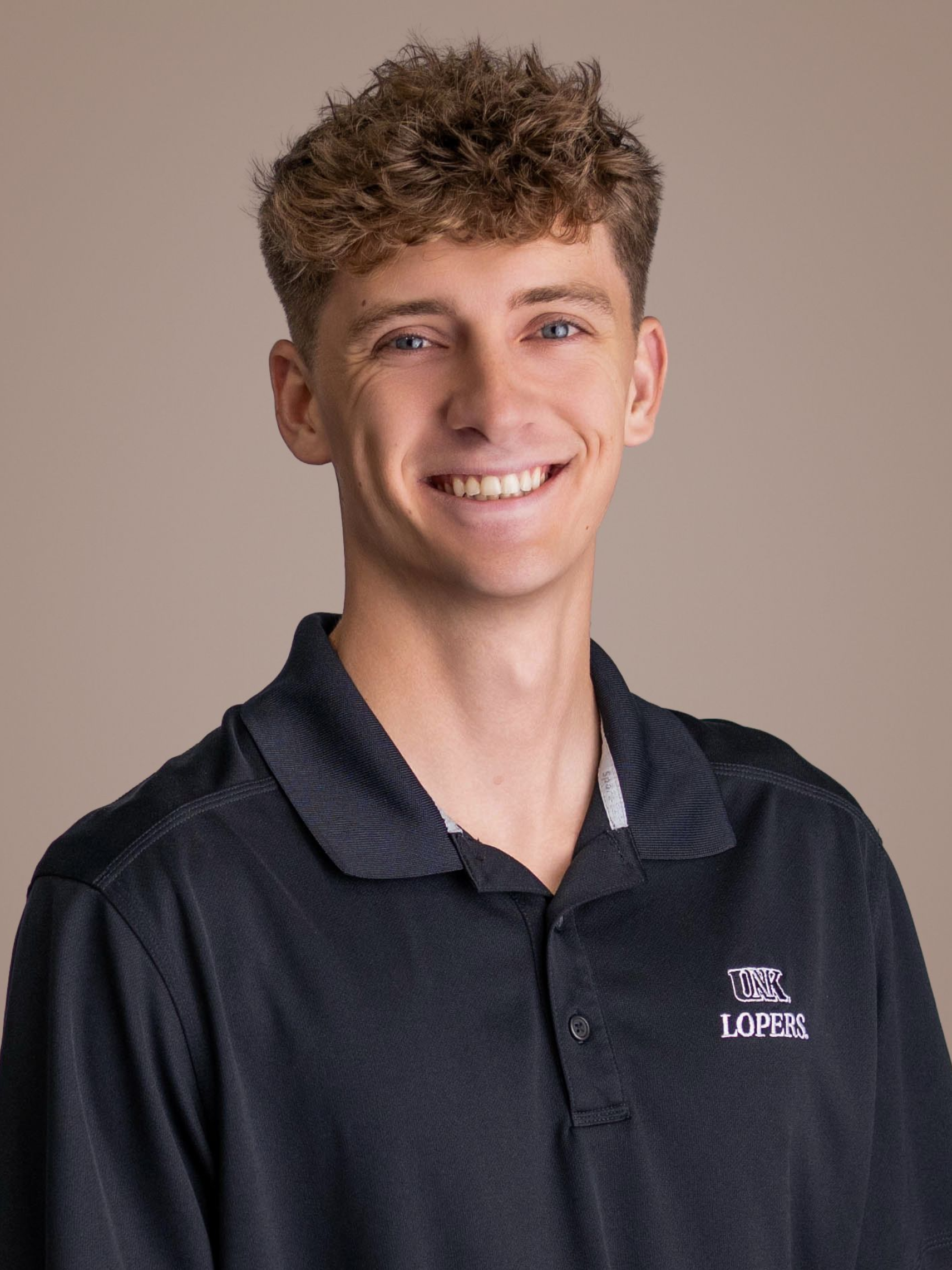 Smiling person in a dark polo shirt against a plain beige background
