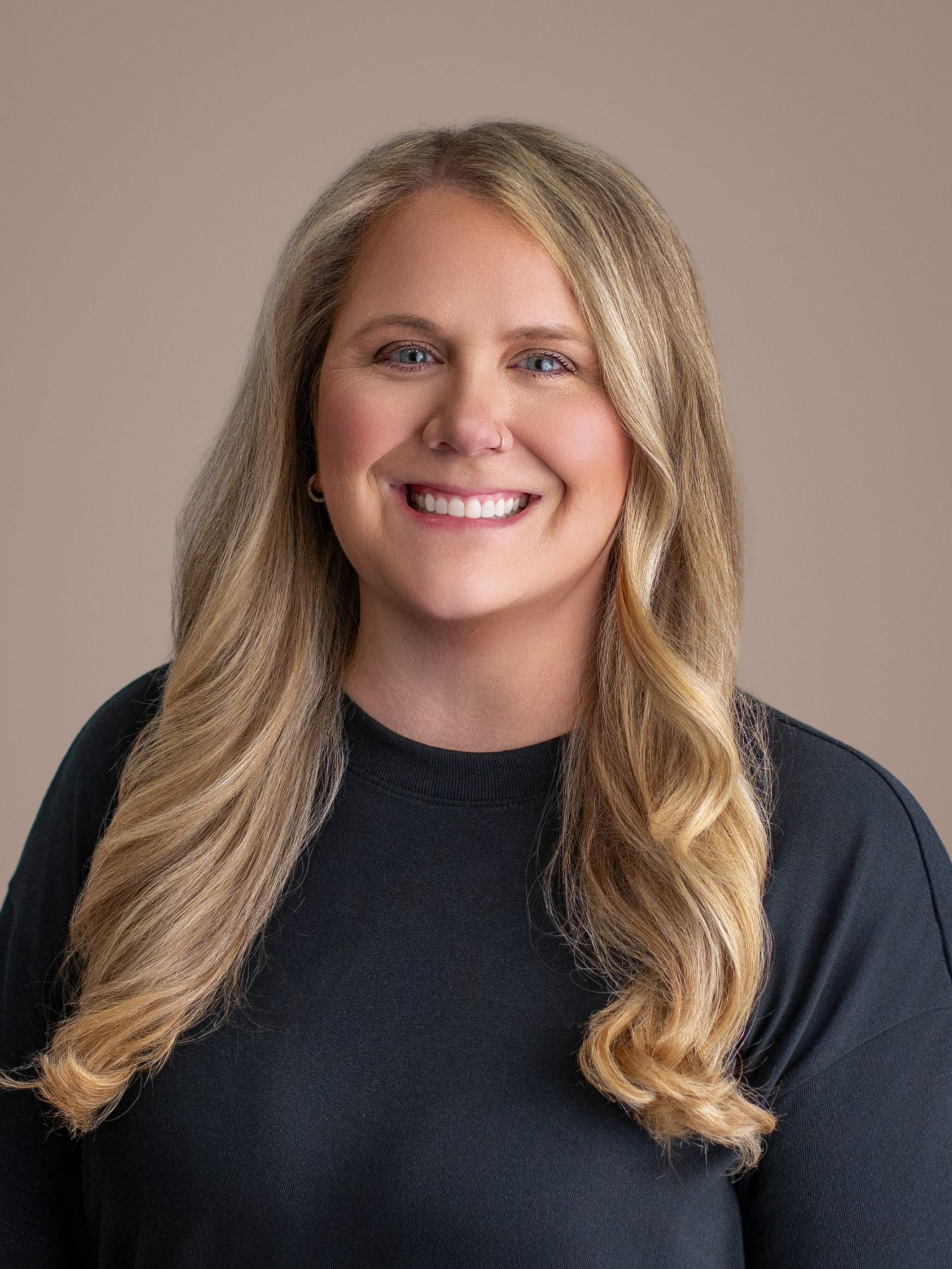 Smiling woman in a dark top against a plain beige background