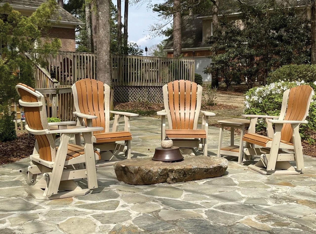 Four wooden chairs around a stone fire pit on a patio, with trees and a house in the background.