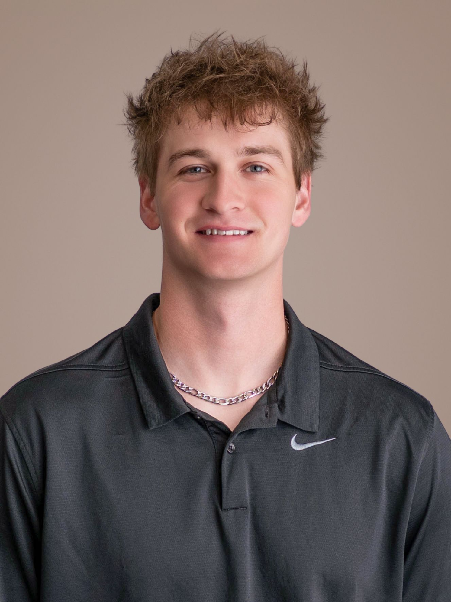 Smiling person in a dark gray Nike polo against a plain beige background