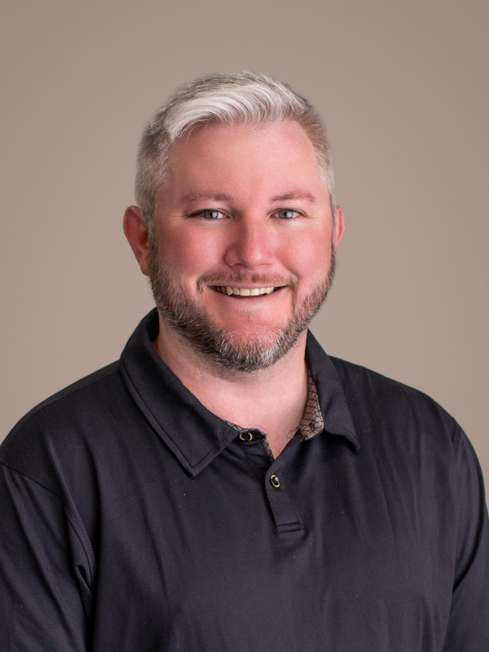 Smiling man in a dark polo shirt against a plain beige background