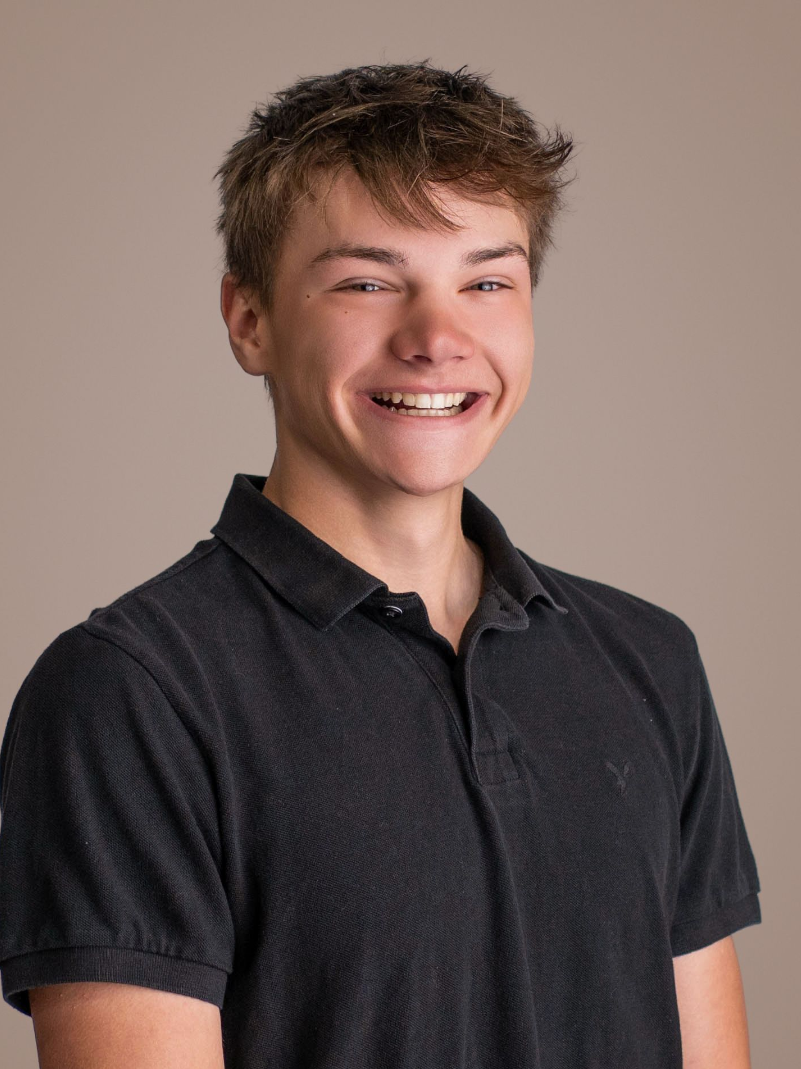Smiling person in a dark gray polo shirt against a plain beige background