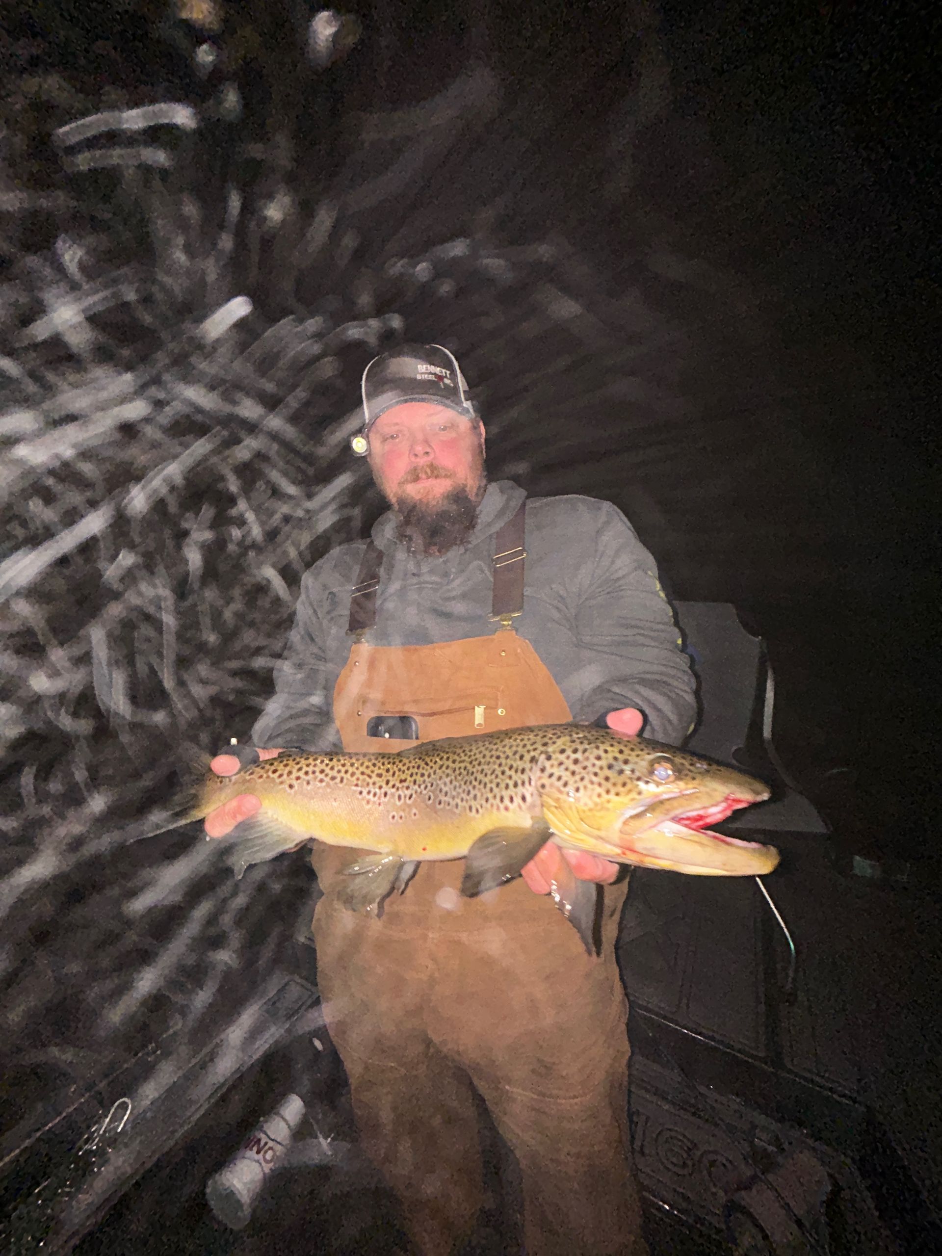 Person in waders holding a large fish at night, with water splashing around them.