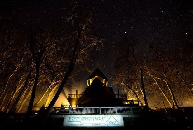 Illuminated house at night with trees silhouetted against a starry sky