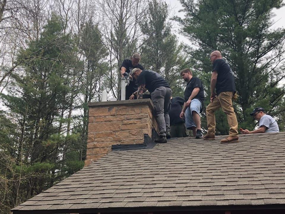 A group of men are working on a chimney on top of a roof.