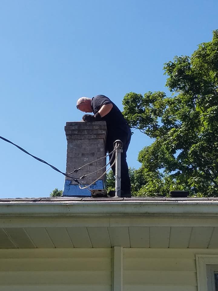A man is working on a chimney on the roof of a house.