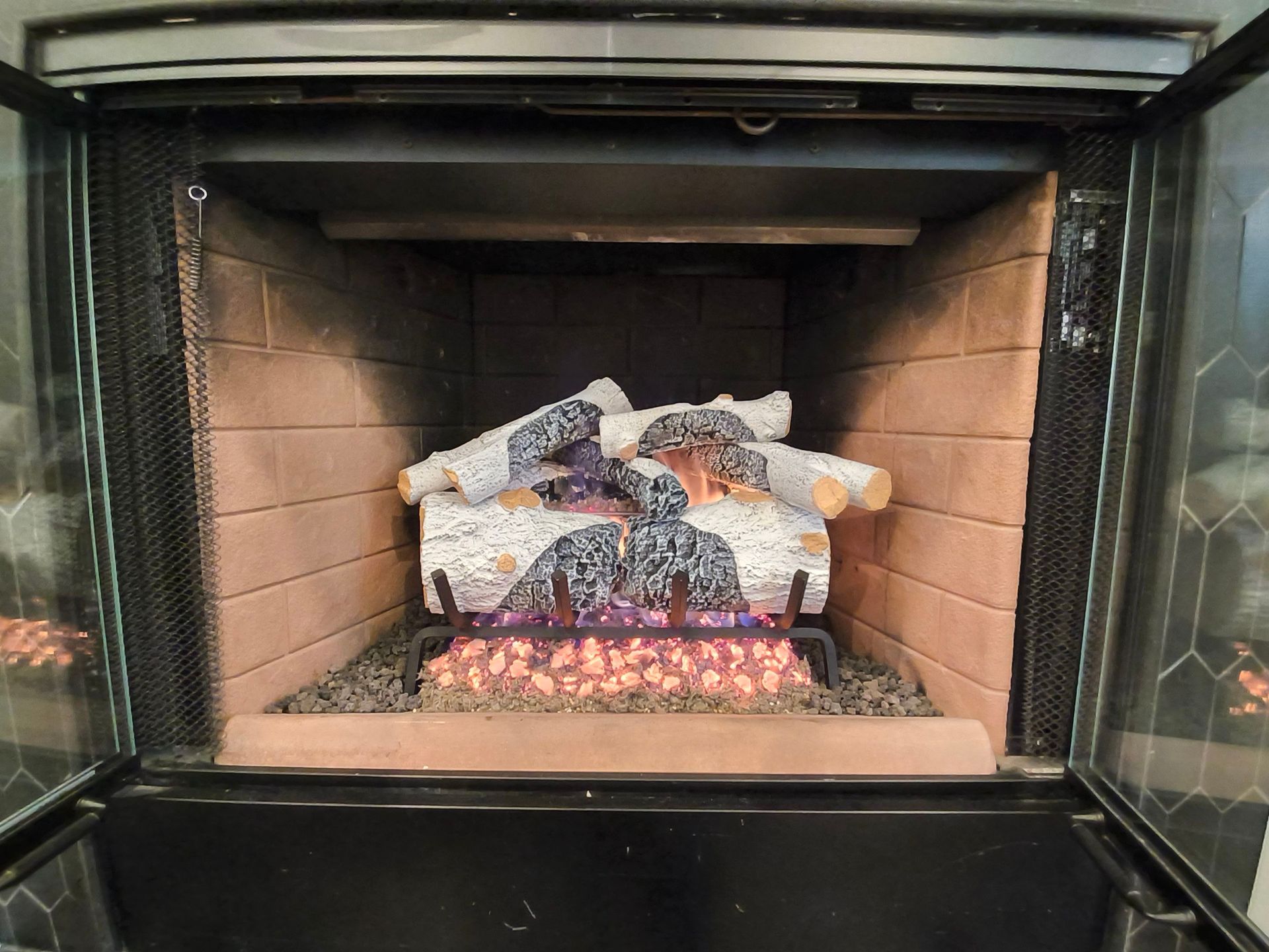 Brick fireplace with an artificial log and ember fire display inside an open glass door.