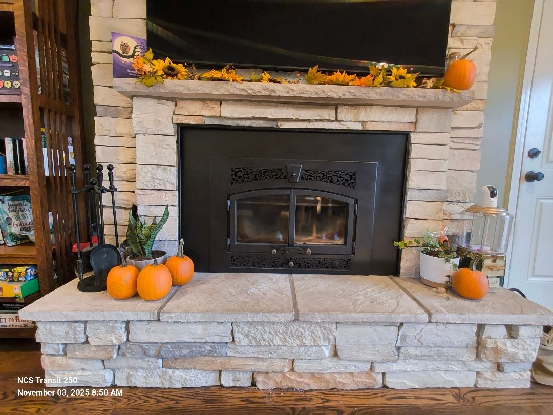 Stone fireplace with black wood stove, autumn garland, and pumpkins on the hearth and mantel
