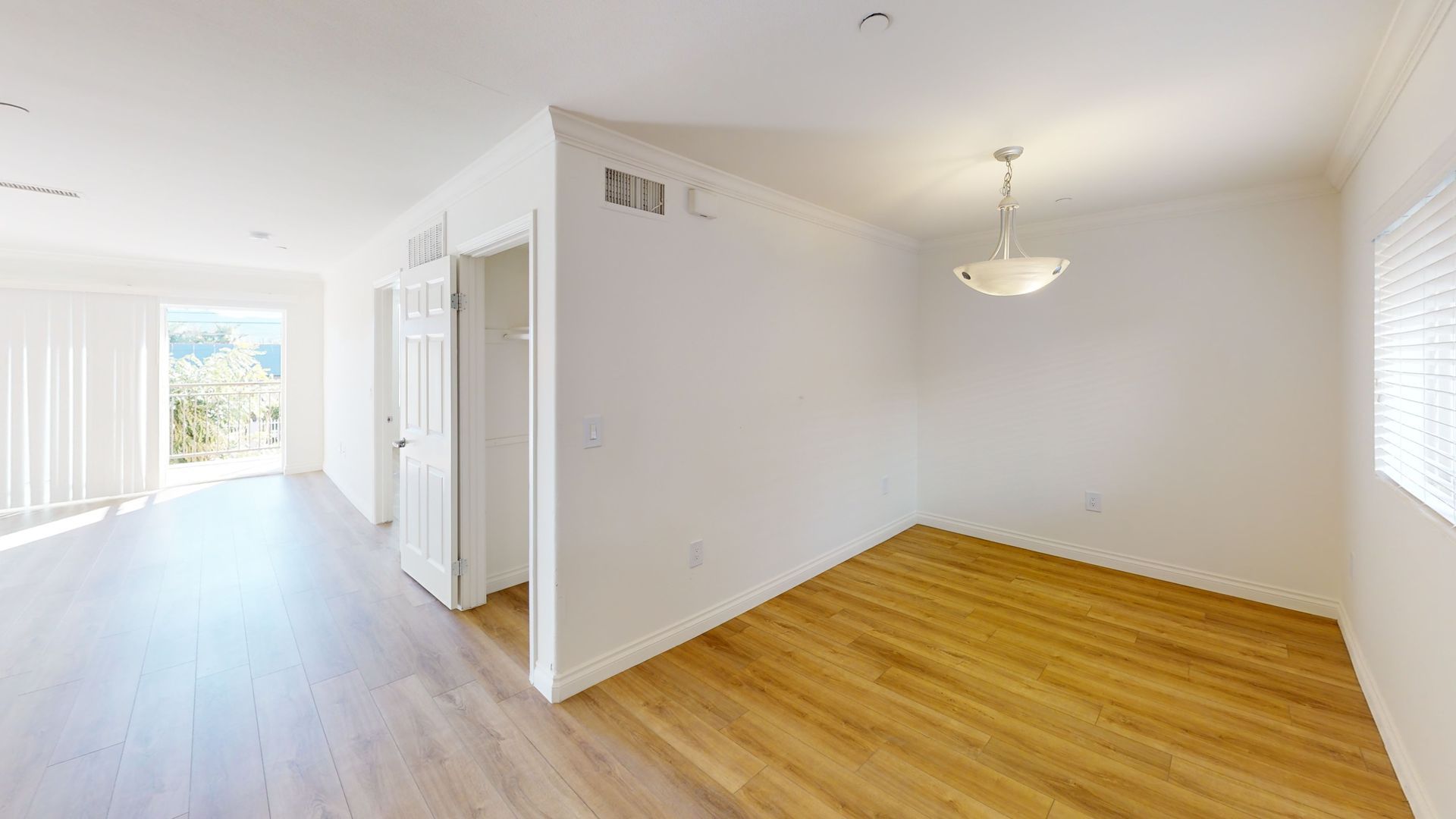 Empty, well-lit interior room with wooden floors, white walls, closet, and a light fixture.