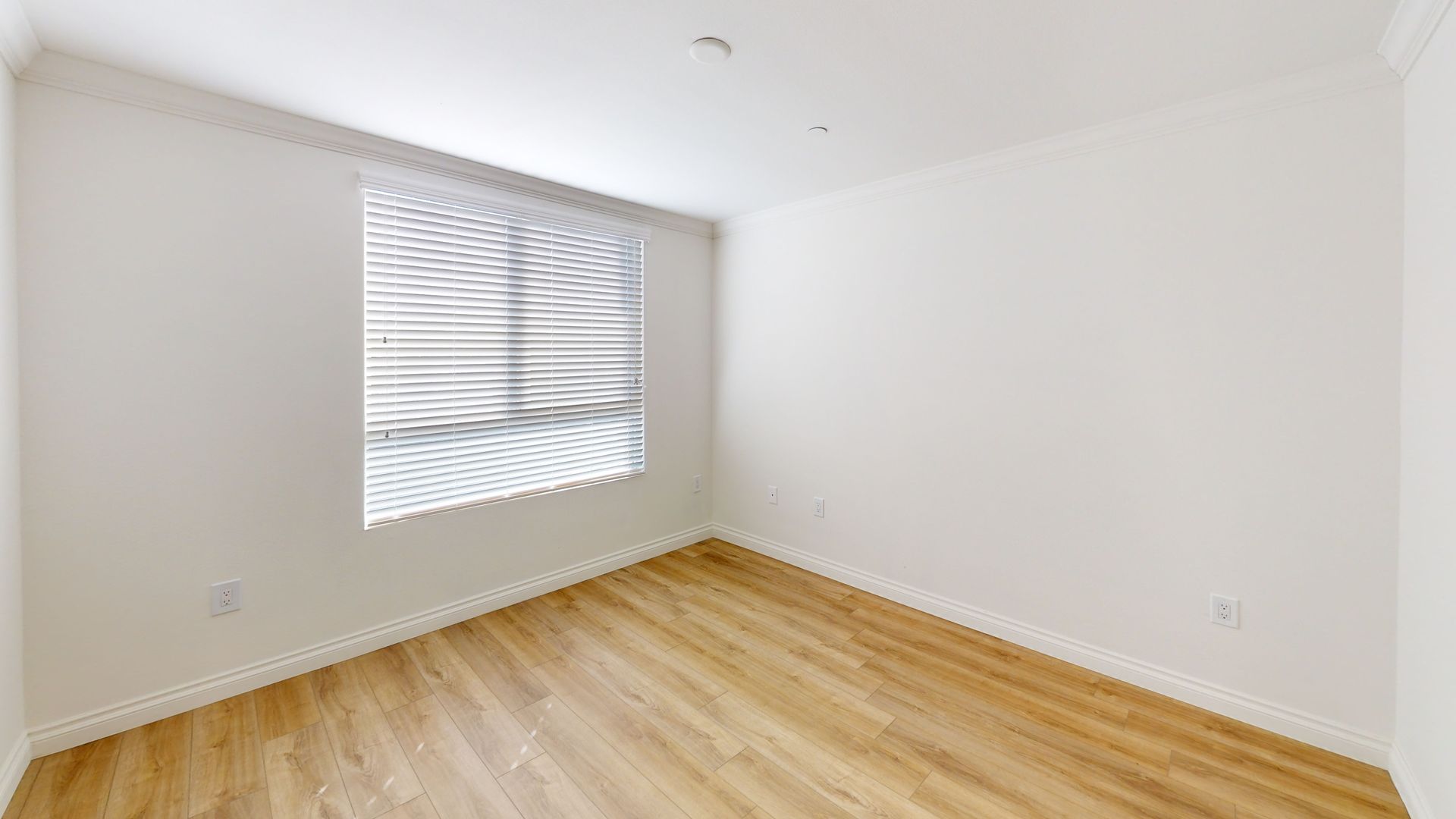 Empty, white-walled room with a window, blinds, and wood-look flooring.