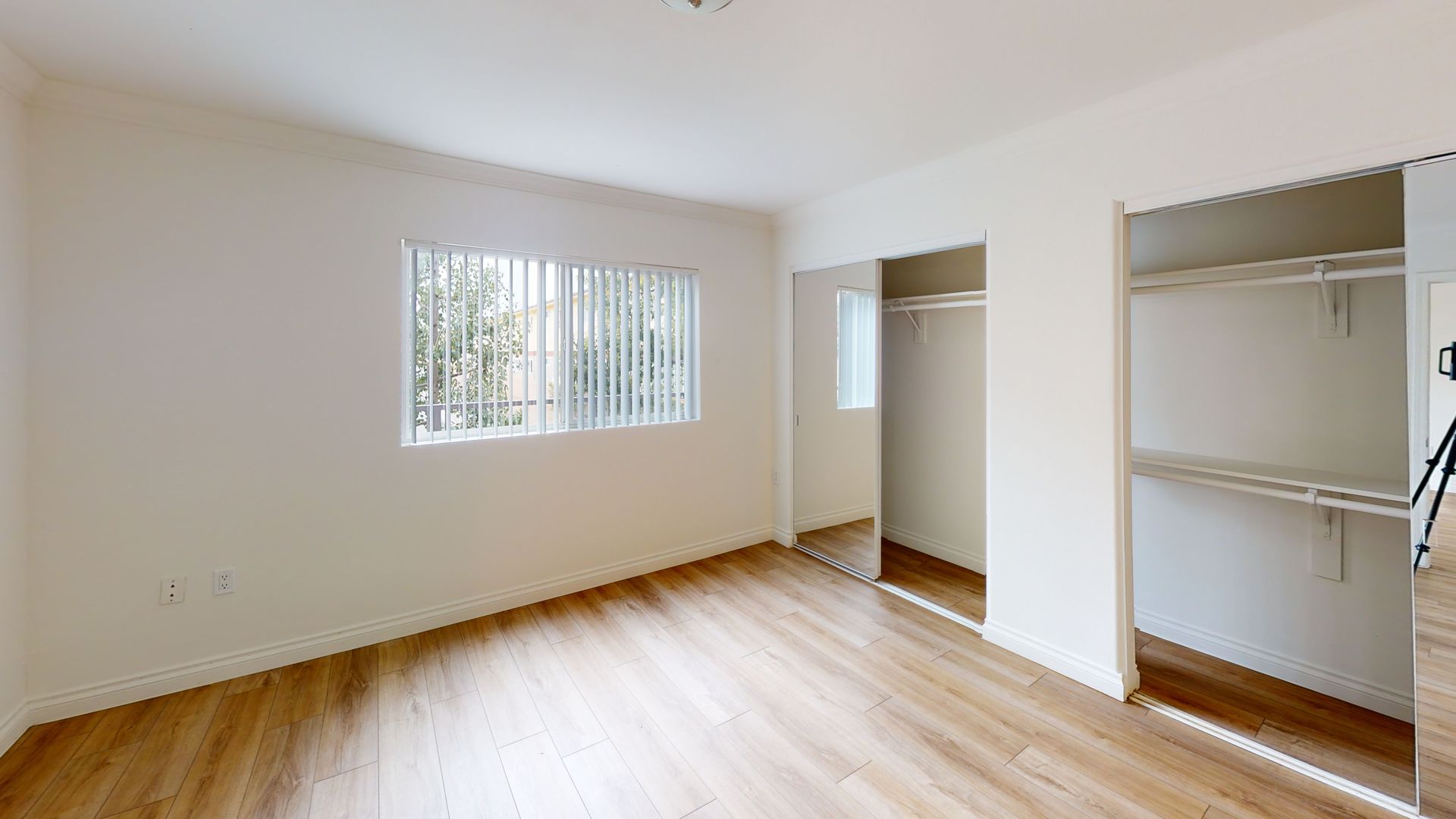 Empty bedroom with wooden floor, white walls, closet, and window.