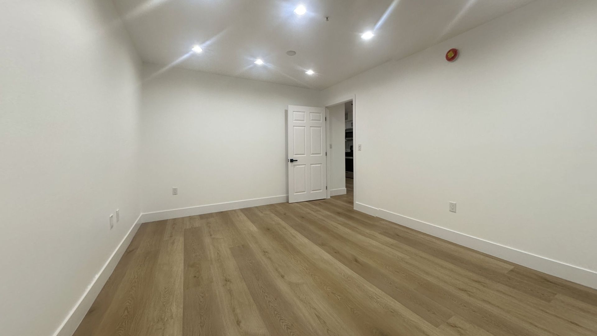 Empty room with light wood floors, white walls, and a closed door.