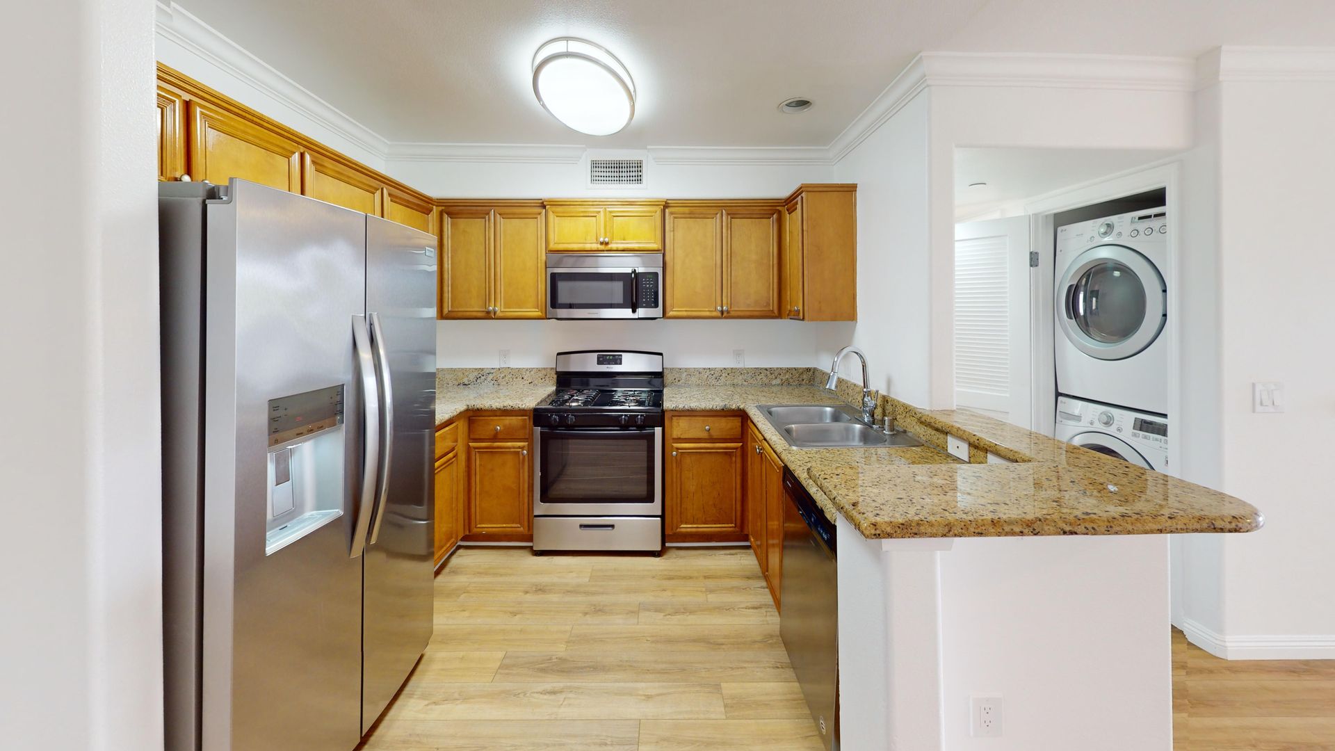 Kitchen with stainless steel appliances, light wood cabinets, granite countertops, and a washer/dryer in the doorway.