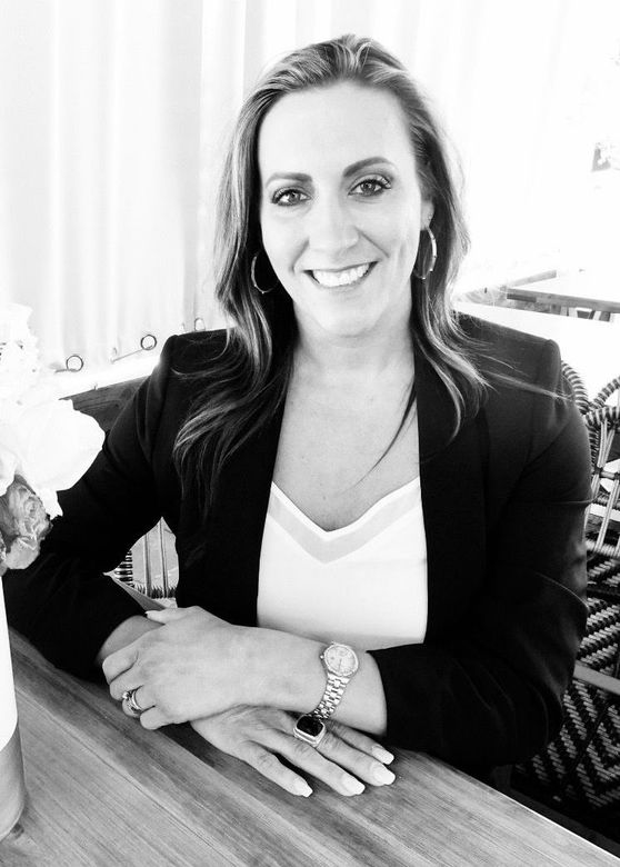 REALTOR, Brooke Pierce, is sitting at a table with her hands folded and smiling in a black and white photo.