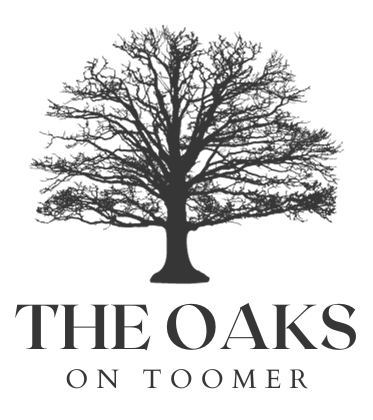 A black and white logo for the oaks on toomer, a luxury development in downtown auburn, alabama