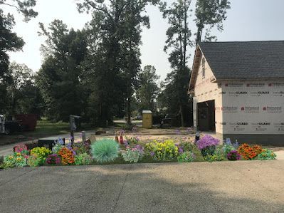 A garden with colorful, fluffy flowers in front of a new house under construction.