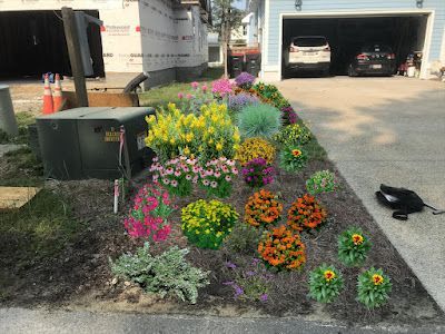 Colorful flower bed in front of a light blue garage, next to a construction site.