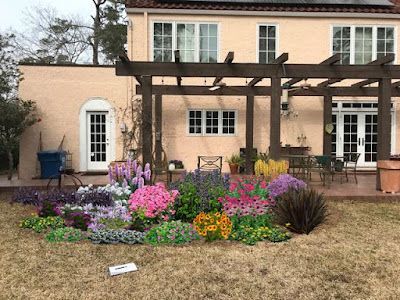 A colorful flower bed in front of a light pink house with a wooden pergola.