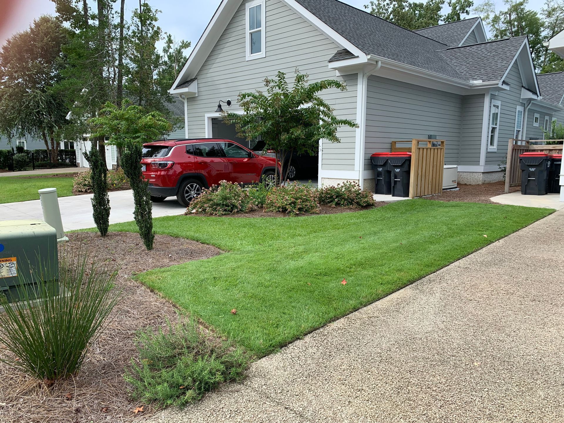 A red SUV parked in front of a gray house with a green lawn.