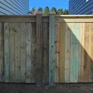 Wooden fence with two posts, varying shades of green and brown, against a blue sky.