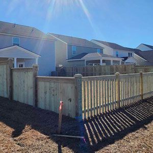 Wooden fence in a sunny backyard with several houses visible in the background.