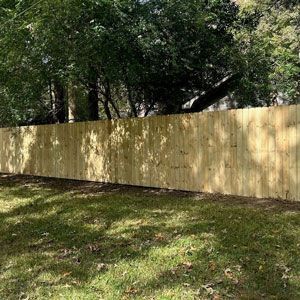 Wooden fence in a grassy yard, with trees in the background.