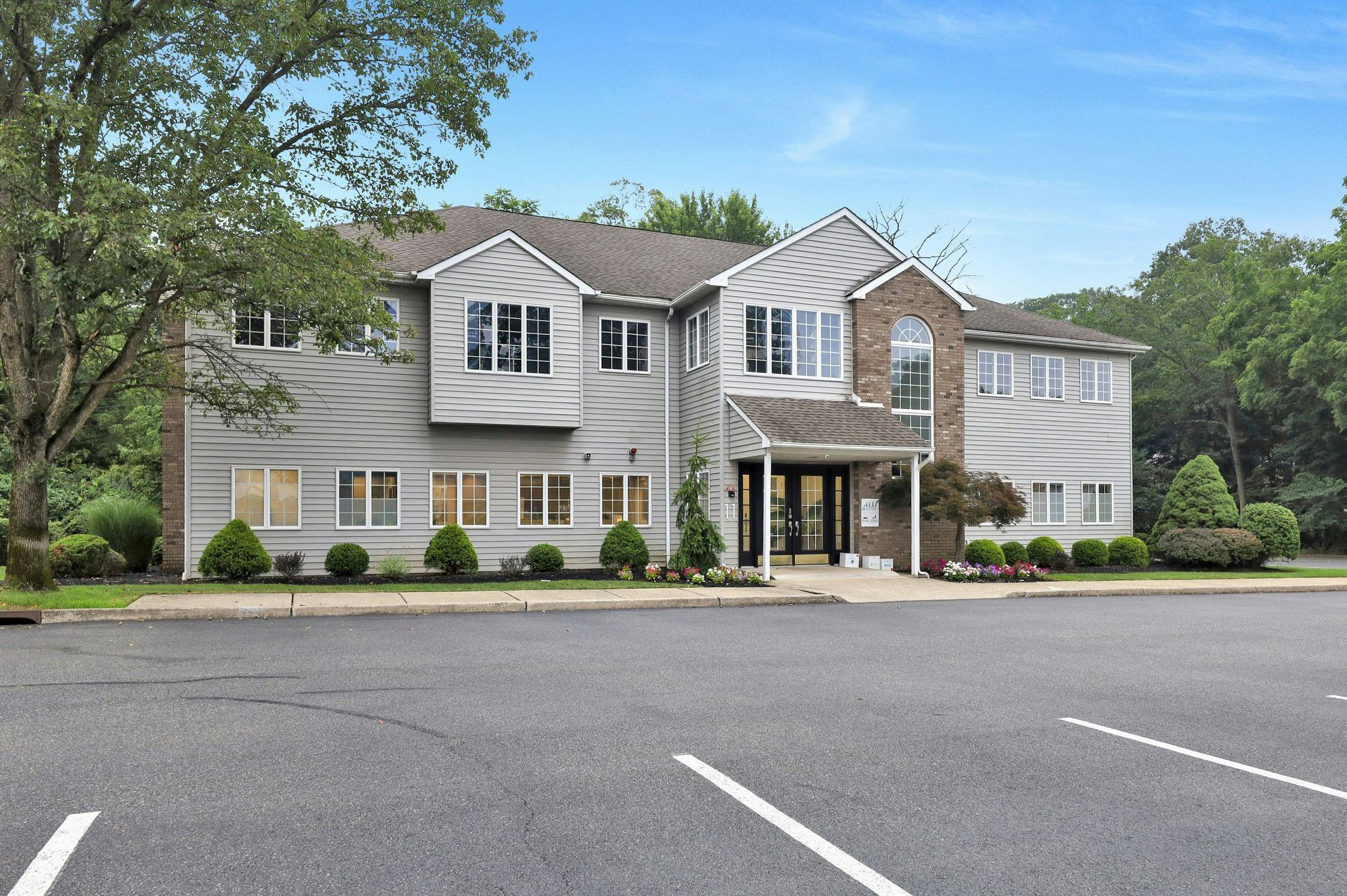 Gray two-story building with a brown roof. Parking lot in front. Cloudy blue sky.