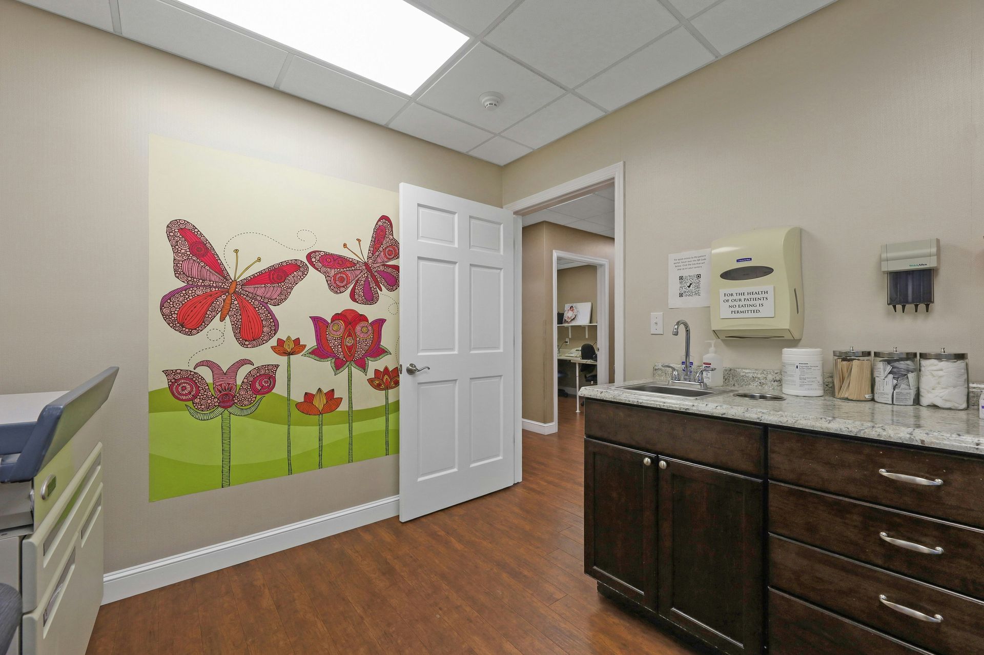 Exam room with butterfly artwork, sink, cabinets, and a doorway.