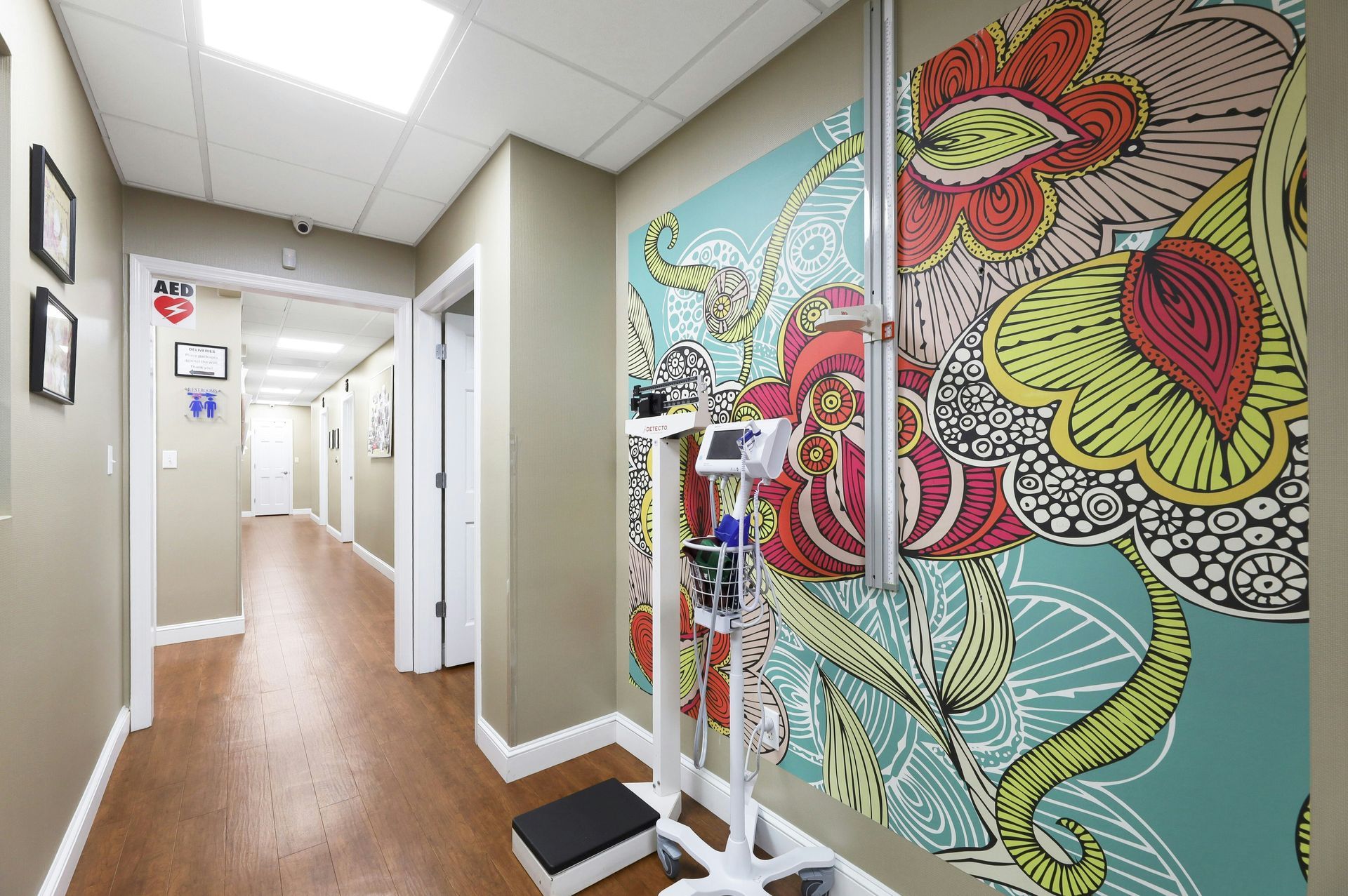 Hallway in a medical office, with floral patterned wall, medical scale, and doors.