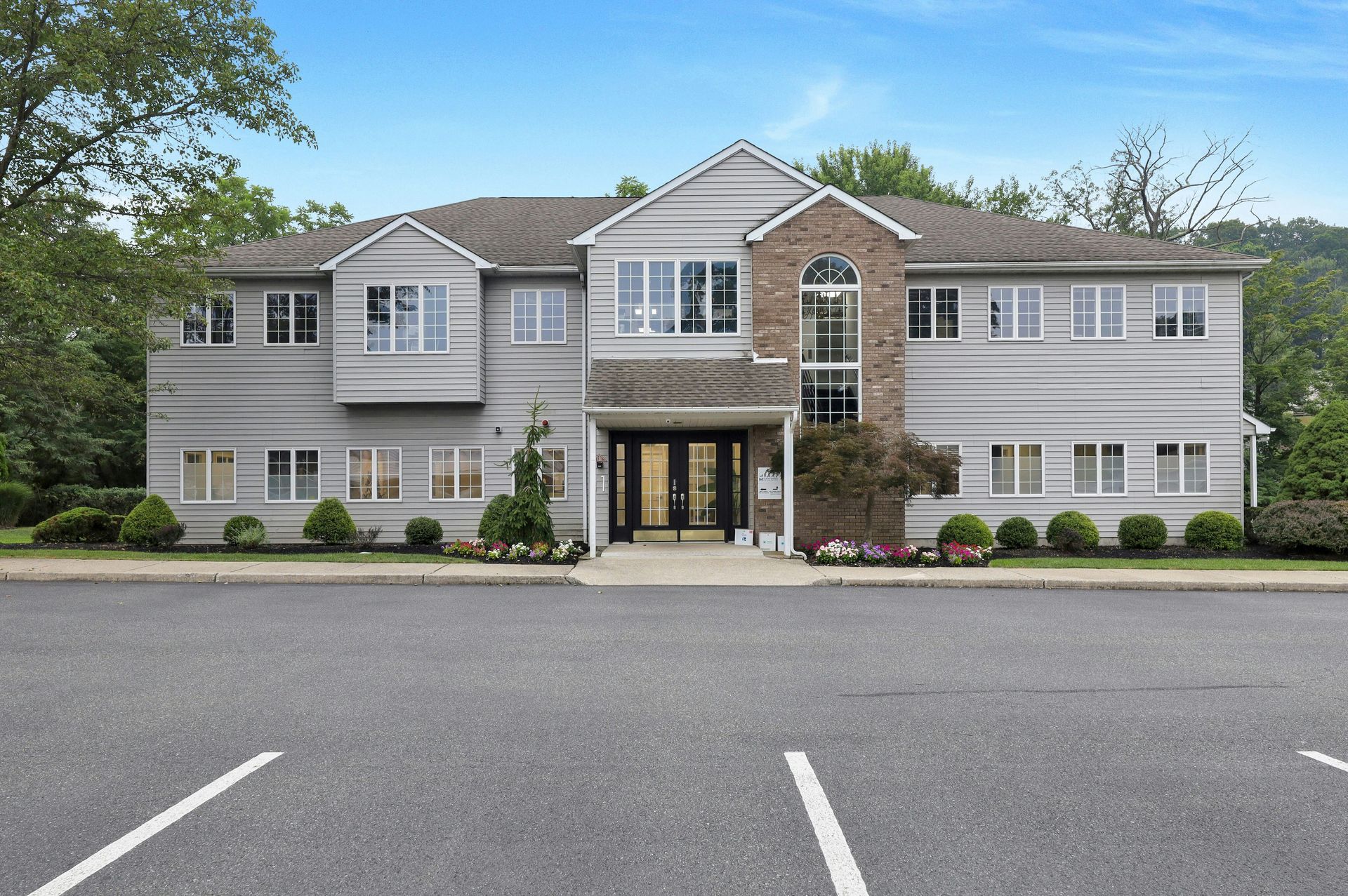 Multi-story commercial building with gray siding, brick accents, and a paved parking lot.