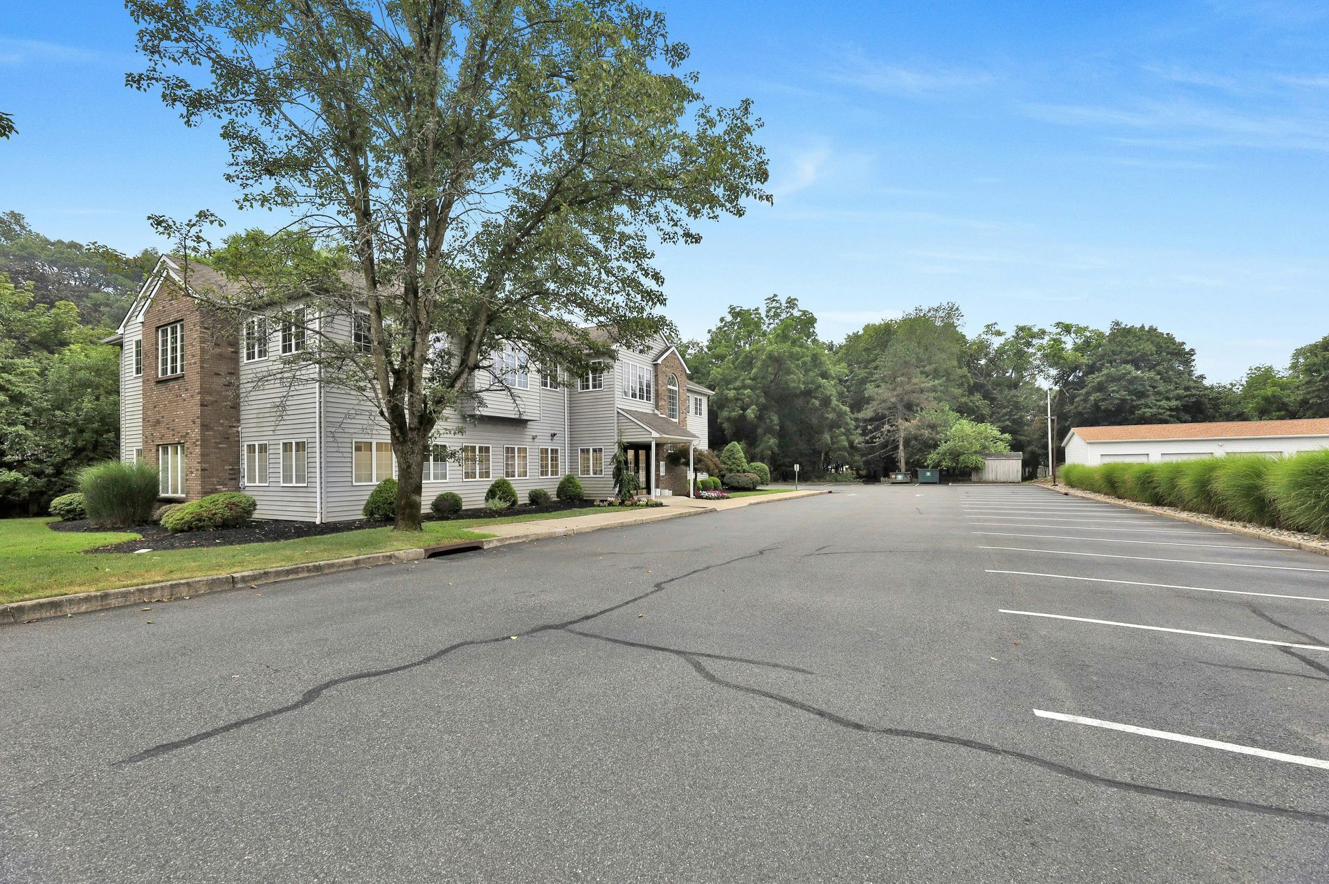 Building with a large parking lot on a sunny day. Trees and shrubs surround the building.