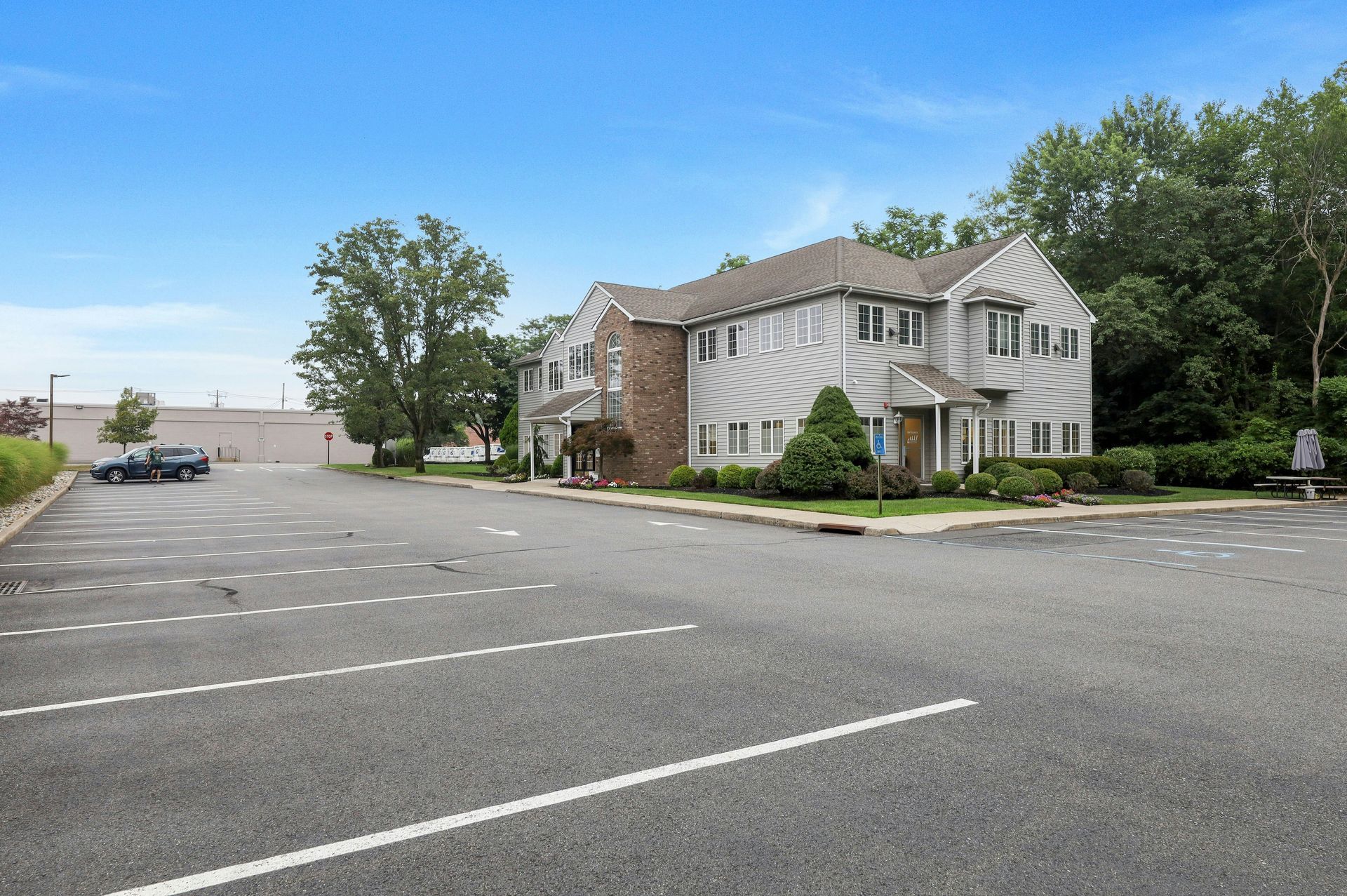 Building with parking lot; two-story structure, gray siding, brown brick chimney, blue door, blue sky.